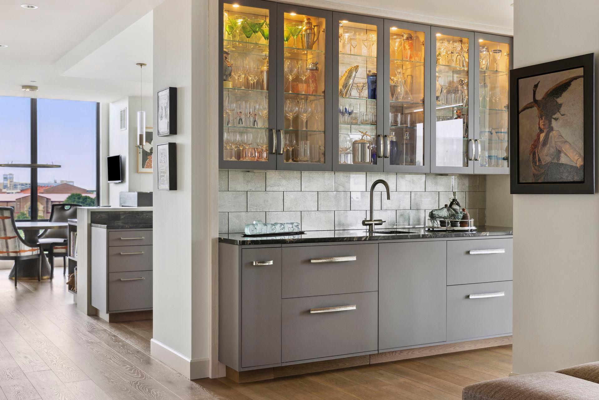 The granite topped wet bar is backed with sparkling silver glass tiles. Interior cabinet lighting can create different scenes. The bar includes integrated Sub-Zero refrigerated/ice maker drawers.