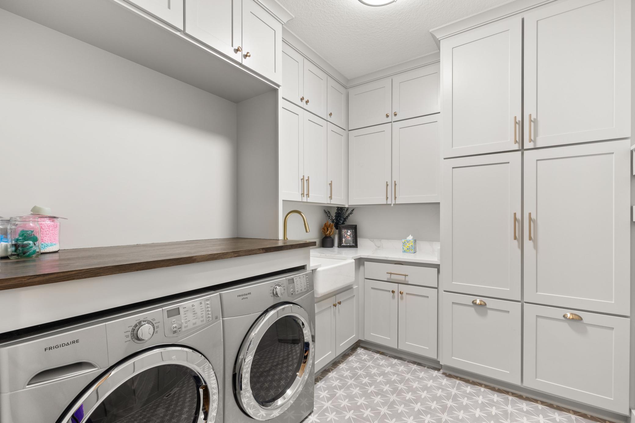 Freshly updated laundry room offers plenty of storage in the built-in cabinets, folding table & a farmhouse sink