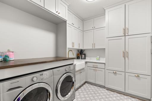 Freshly updated laundry room offers plenty of storage in the built-in cabinets, folding table & a farmhouse sink