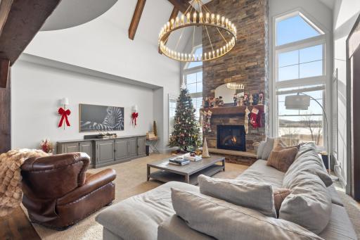 Exquisite 2-story vaulted living room features stone fireplace, modern chandelier, beamed ceiling and gorgeous windows offering spectacular views of the backyard