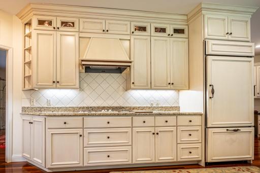 Main level kitchen features Brazilian walnut flooring, under cabinet lighting, granite countertops, paneled dishwasher, paneled commercial refrigerator, center island, and a tile backsplash.