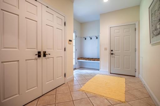 Mudroom off of the garage entrance features a bench with coat hooks, storage closet, access to the backyard, and tile flooring.