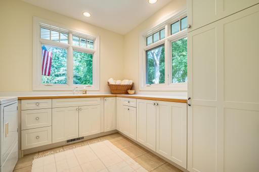 Large main floor laundry room with storage and countertops, tile flooring, and recessed lighting.