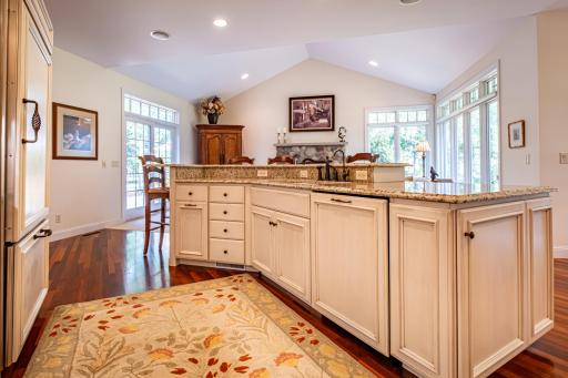 Main level kitchen features Brazilian walnut flooring, under cabinet lighting, granite countertops, paneled dishwasher, paneled commercial refrigerator, center island, and a tile backsplash.
