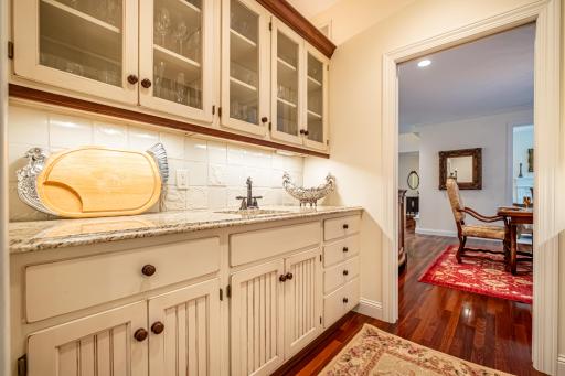 Butler's pantry with walk-through access to the formal dining room features a sink with hot and cold water and under cabinet lighting.