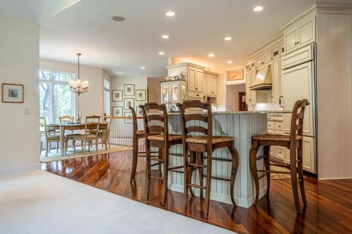 Main level kitchen features Brazilian walnut flooring, under cabinet lighting, granite countertops, paneled dishwasher, paneled commercial refrigerator, center island, and a tile backsplash.