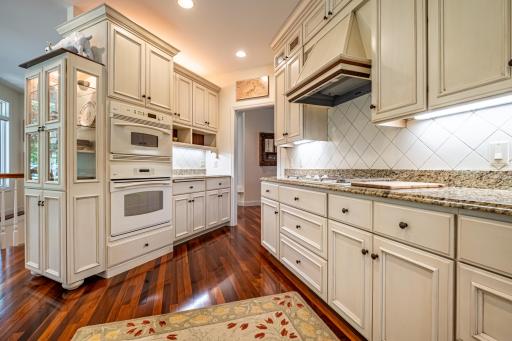 Main level kitchen features Brazilian walnut flooring, under cabinet lighting, granite countertops, paneled dishwasher, paneled commercial refrigerator, center island, and a tile backsplash.