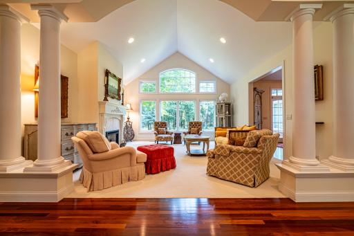 Main floor formal living room features a gas burning fireplace, vaulted ceilings, large windows, and pillars.