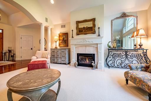 Main floor formal living room features a gas burning fireplace, vaulted ceilings, large windows, and pillars.