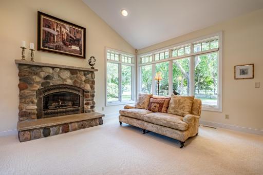 Informal living room features a stone gas burning fireplace, vaulted ceiling, recessed lighting, and large picture windows.
