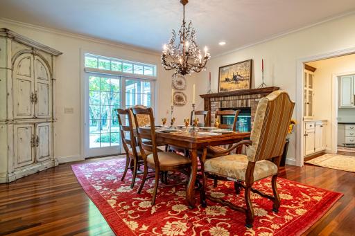 Formal dining room features a brick wood-burning fireplace, Brazilian wood flooring, a patio door to the backyard, and a large chandelier.