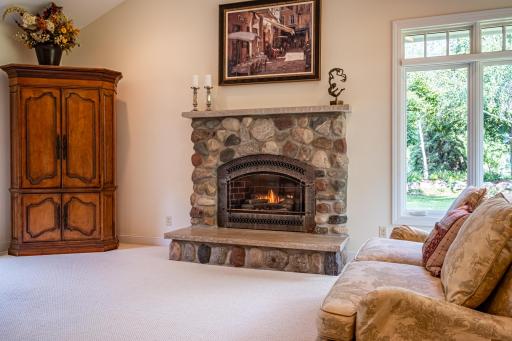 Informal living room features a stone gas burning fireplace, vaulted ceiling, recessed lighting, and large picture windows.