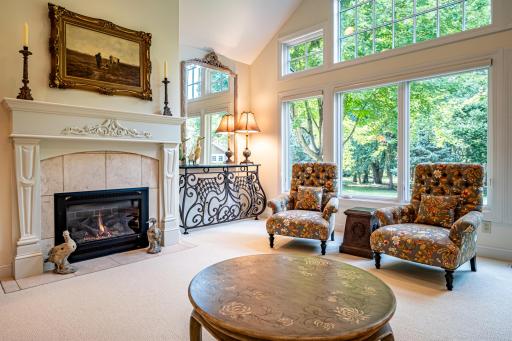 Main floor formal living room features a gas burning fireplace, vaulted ceilings, large windows, and pillars.