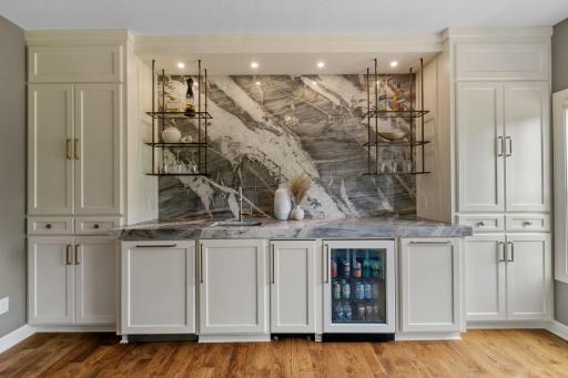 Built-in wet bar features enameled cabinetry, stunning quartzite countertop and full slab backsplash, Granite composite sink, metal display shelving