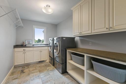 Abundance of enameled cabinets feature open shelving for baskets, large folding counters and drop-in utility sink with front loading washer and dryer on stands with storage