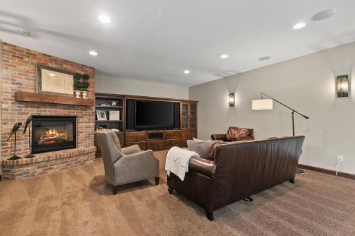 Gas fireplace w/ rustic brick surround and raised hearth and built-in entertainment cabinets feature glass doors, open display shelving, storage and large opening for a modern sized TV