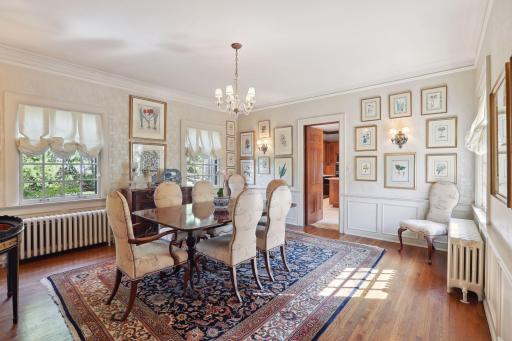 Spacious light-filled formal dining room with wainscoting, hardwood floors, and views of the gardens.