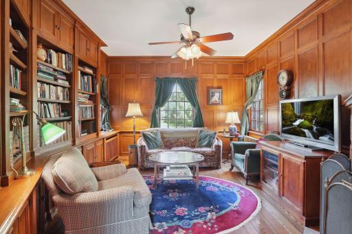 Cozy main level family room or study with wood-paneled walls, wood burning fireplace, and built-in library shelving. Views to the yard and gardens.