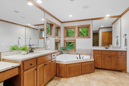 Dual vanities w/ additional make-up counter and granite tops & a corner jetted tub situated on a tile deck and surround in the Master Bathroom