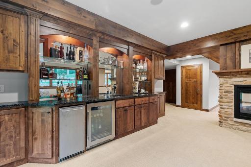 Wet bar features rustic alder cabinetry, glass display shelves w/ accent lighting, granite countertops, roll-out storage, ice maker and beverage refrigerator