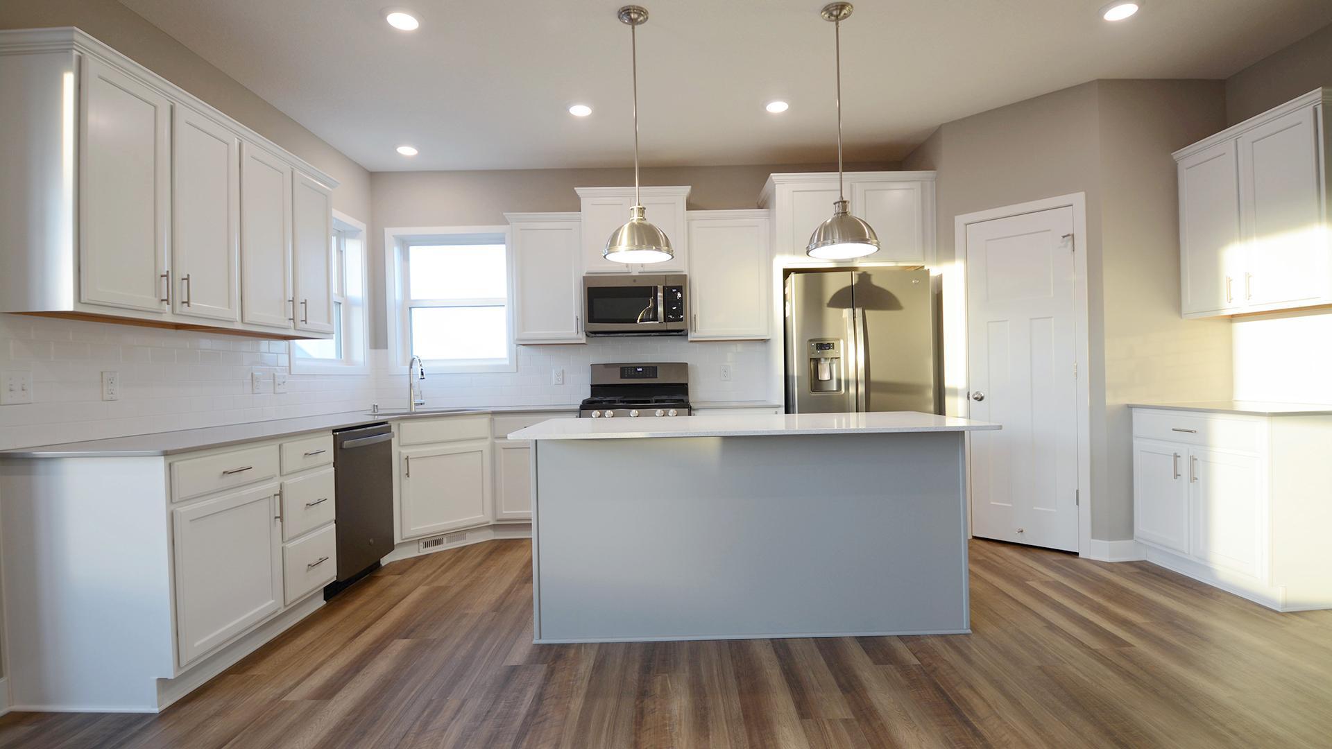 The kitchen is home to a large center island complete with quartz countertops, stainless appliances and a luxurious gas cooktop. (Photo of completed home, actual home finishes may vary slightly)