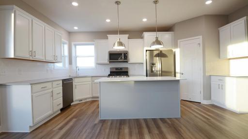 The kitchen is home to a large center island complete with quartz countertops, stainless appliances and a luxurious gas cooktop. (Photo of completed home, actual home finishes may vary slightly)