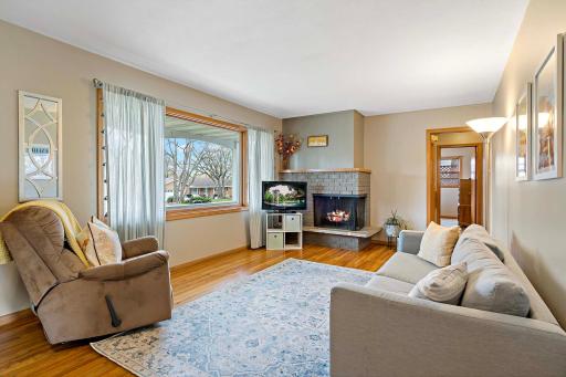 A warm and inviting living room on the main level features beautiful flooring, a large window for plenty of daylight and a brick fireplace to cozy up in the cooler months.