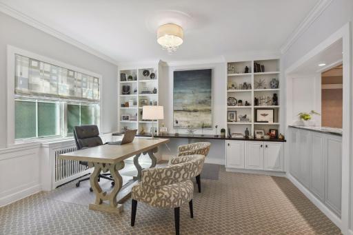 Main level den/office adjacent to living room and dining room. Built-in library shelving and desk area. An open counter looks into the dining room.