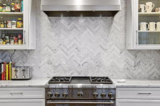 Marble herringbone backspash behind the range. Exhaust hood.