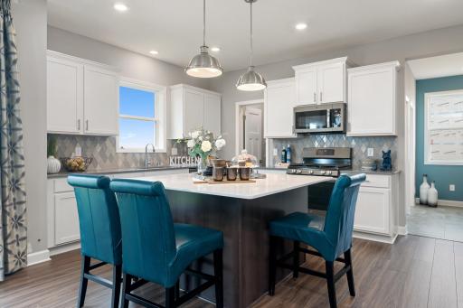 Welcome to the Taylor! This spacious kitchen features a large pantry, quartz kitchen counters, recessed lighting, LVP wood floors, stainless appliances and more. (Photo of decorated model, actual home's finishes may vary slightly)