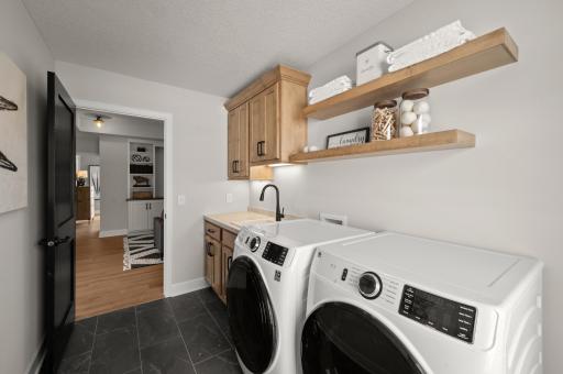 The upper level laundry room has a drop in sink, additional cabinets and floating shelves.
