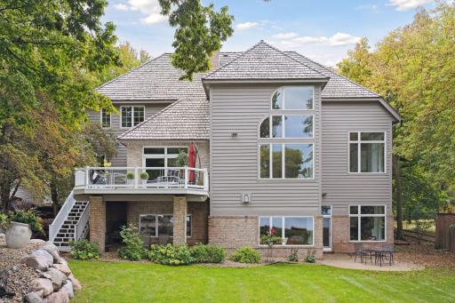 Lakeside views showcasing the home's gorgeous aesthetics. Natural boulder rock wall landscape & mature trees frame the views of the shoreline. Expand your living space to the large upper deck & exposed aggregate patio.