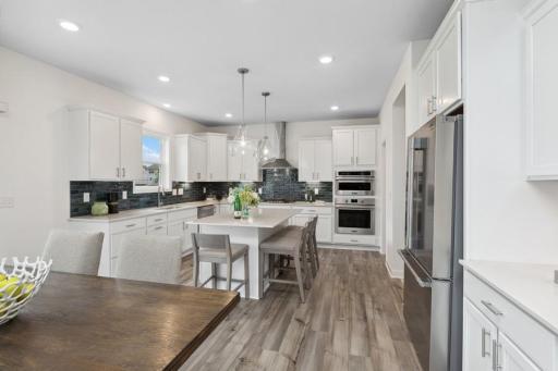 This spacious kitchen features a large center island, quartz countertops, recessed lighting, LVP wood floors, stainless appliances and more! (Photo of decorated model, actual home's finishes may vary slightly)