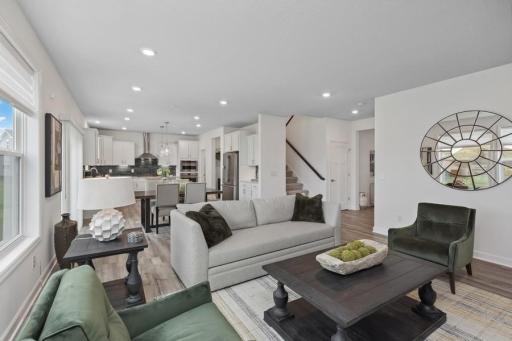 The spacious living room seamlessly connects the kitchen area, perfect for entertaining. It also features many large windows providing warm natural light. (Photo of decorated model, actual home's finishes may vary slightly)