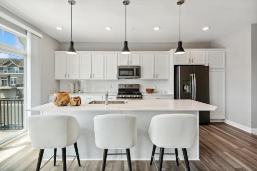 The kitchen is home to a large center island complete with quartz countertops, stainless appliances, LVP wood flooring and more! (Photo of decorated model, actual home's finishes may vary slightly)