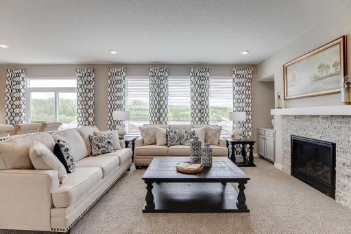 The family room is punctuated by a gas fireplace - which serves as a cozy bookend to the area and highlights a space that's flooded in natural light via these three soaring windows! Photo of model home, color and options will vary.