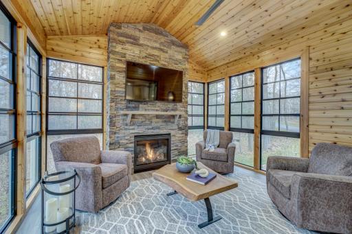 Relax and unwind in the cozy three season porch with floor to ceiling stone gas fireplace surrounded by floor to ceiling windows