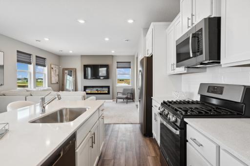 Welcome to the Biscayne! This spacious kitchen features a large center island, quartz countertops, under mount sink, recessed lighting, LVP wood floors, stainless appliances and more. (Photo of decorated model, actual home's finishes may vary)