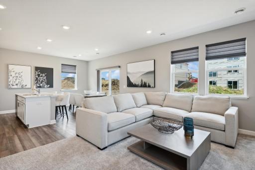 This spacious family room seamlessly connects to the kitchen area, perfect for entertaining. It also features many large windows providing warm natural light. (Photo of decorated model, actual home's finishes may vary slightly)