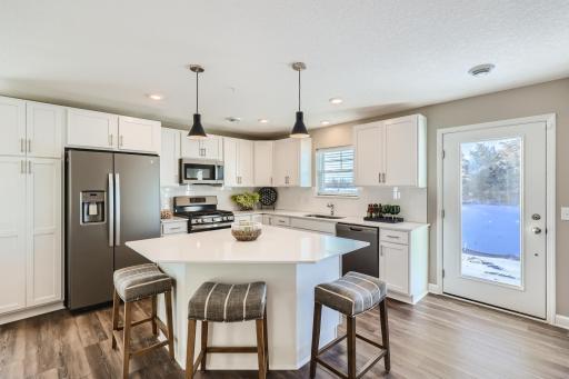 The kitchen is home to a large center island complete with quartz countertops, stainless appliances and a luxurious gas cooktop. (Photo of decorated model, actual home finishes may vary slightly)