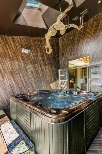 An incredible indoor/outdoor hot tub room features floor to ceiling tile featuring custom sparkly grout
and a stunning artistic light fixture.