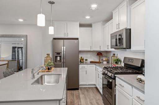 This kitchen is home to a large center island complete with granite countertops, stainless appliances, LVP wood floors and more! (Photo of decorated model, actual home's finishes may vary slightly)