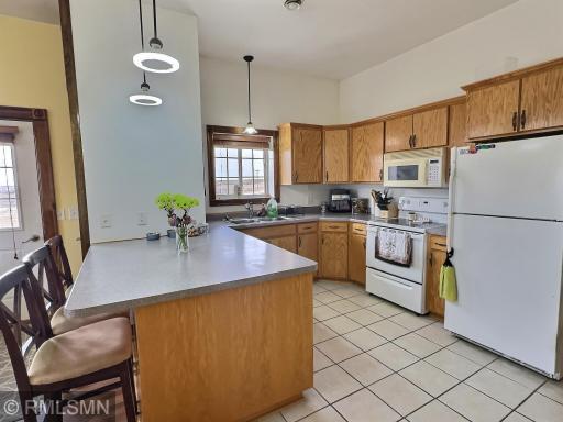 The kitchen includes tile flooring, pendent lights, window, breakfast bar, stove, refrigerator and microwave.