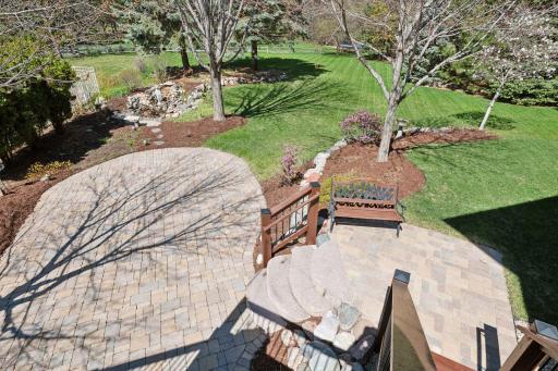 Outdoor amenities include an inviting front porch, spacious deck, paver patio, boulder accents, and a water feature surrounding lush landscaping.