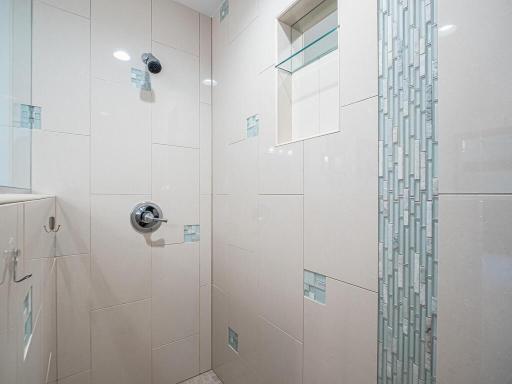 Remodeled primary ensuite step-in shower with floor-to-ceiling tile and recessed shelving.