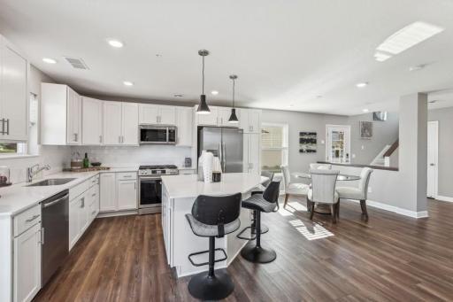Photo for 21942 Primrose Path, Farmington, MN 55024 - Listing #6486300 Designer kitchen with white cabinetry, quartz countertops, slate-finish appliances, gas stove, large center island, backsplash and deep sink. (Photo of decorated model, actual home's finishes may vary slightly)