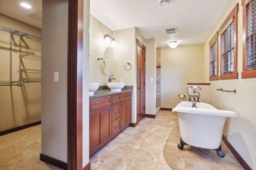 Indulge in luxury in the primary bathroom featuring granite counters, windows with wooden blinds, tiled shower, and elegant claw-footed bathtub. Complimented by a spacious walk-in closet.