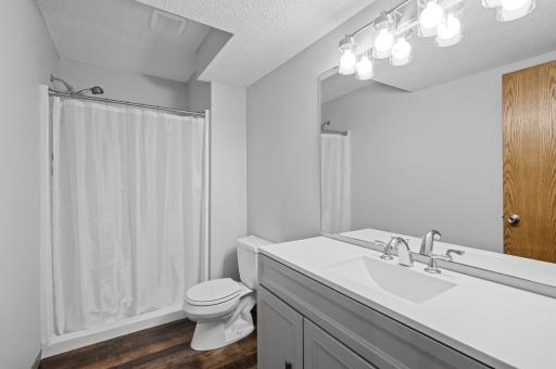 The lower level three-quarter bathroom has been completely remodeled with gorgeous luxury vinyl plank flooring, an oversized vanity with a solid surface top, new lighting, and a walk-in shower.