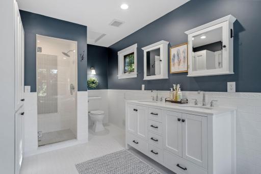 Walk-in shower features subway tile walls, decorative herringbone accent tile, shampoo niche & glass door