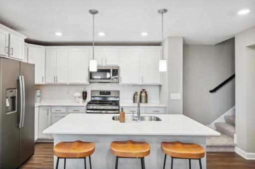 Welcome to your new home! This spacious kitchen features a large center island with quartz countertops, under mount sink, recessed lighting, LVP hardwood floors, stainless appliances and more! (Photo of decorated model, actual home's finishes vary)